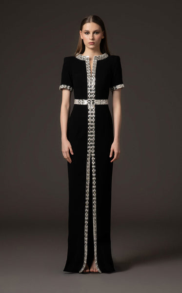 Black evening gown with silver embellishments on a model against a dark background