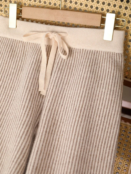 Beige corduroy pants with a drawstring on a hanger against a patterned wall.