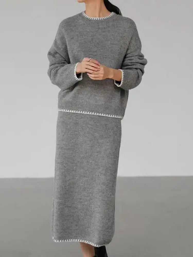 Person wearing a gray sweater and skirt set against a plain background