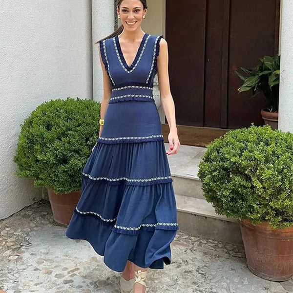 Woman wearing a blue dress with white trim standing outdoors next to potted plants.