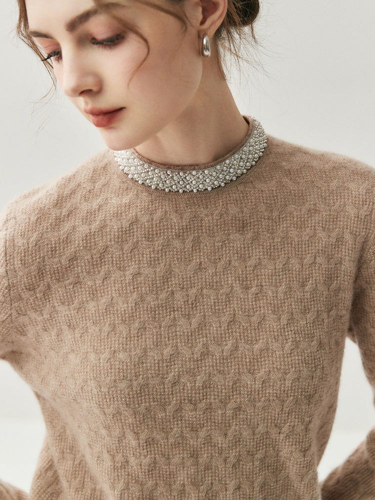 A woman wearing a camel colored 100% cable knit cashmere pullover sweater adorned with small pearls & beads around the half collar 