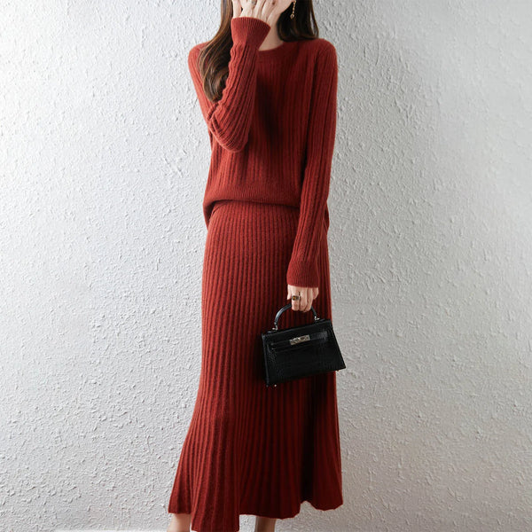 Person wearing a red knit outfit holding a black handbag against a white wall