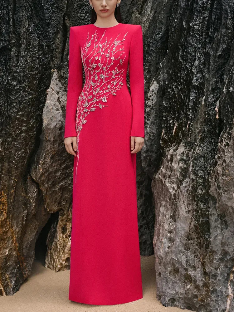 Person wearing a long red dress with silver embellishments standing against a rocky background