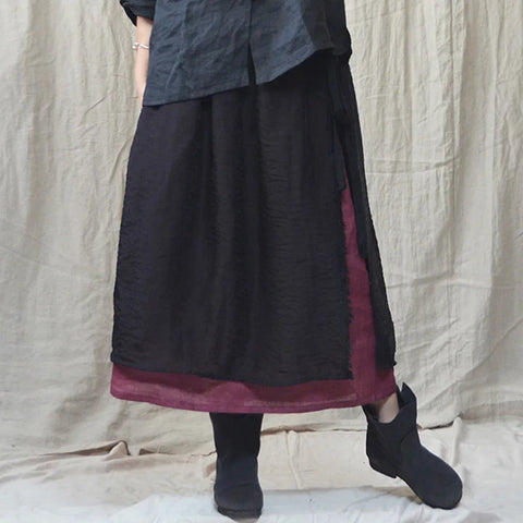 Person wearing a black skirt with a maroon trim against a beige curtain background