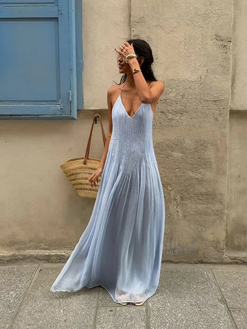 Woman in a light blue dress holding a straw bag against a beige wall.
